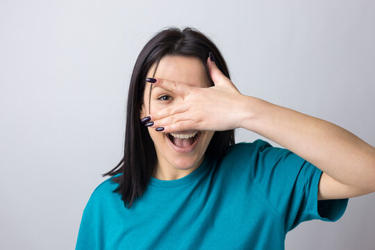 Picture of brunette teenage girl covering face with hands and peeping through her fingers.