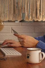 The woman makes online purchases at home on a computer. Workplace at a wooden table in a cozy home. 