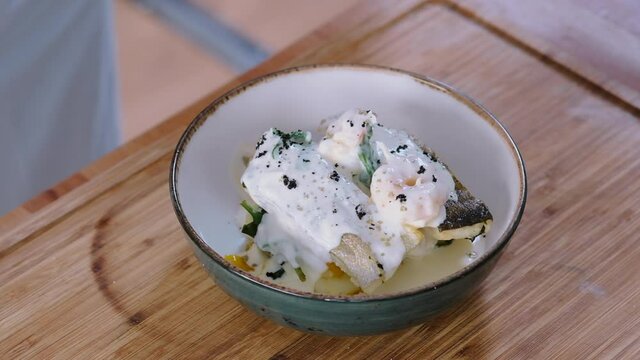 Chef before serving the seafood dish seasons with salt and pepper. Ready to eat prepared main course restaurant meal cod fish garnish vegetables with creamy sauce, close up. Food cooking concept