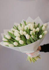 Young woman florist holding big beautiful blossoming mono bouquet of white tulips flowers wrapped...