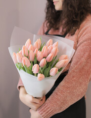 Young woman florist holding big beautiful blossoming mono bouquet of salmon tulips flowers wrapped in paper.