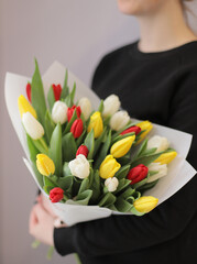 Young woman florist holding big beautiful blossoming mono bouquet of colorful tulips flowers wrapped in paper.