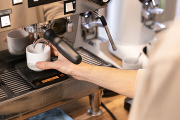 A man makes a fresh espresso in a coffee maker. The barista prepares a hot drink for the clients.