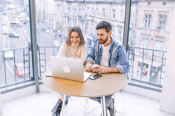 Beautiful couple working on a laptop in a cafe. Happy young man and gorgeous woman smiling, using laptop, sitting at a table in a restaurant.