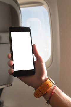 Mockup image of woman's hands holding a black smart phone with blank desktop screen next in the cabin at the window airplane
