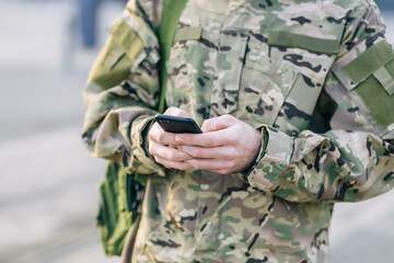 hands of a man holding a mobile phone. A soldier in a camouflage