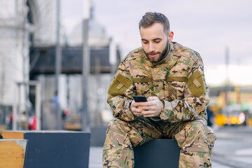 A military soldier sits on a bench at a bus stop waiting for a b