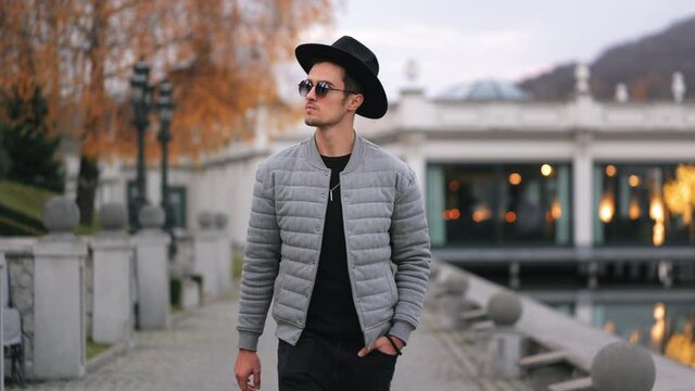 A stylishly dressed man is walking along the quay. He is wearing a hat and sunglasses. 4K