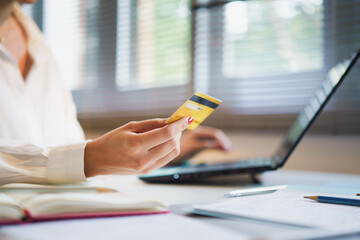 hands of woman holding credit card with blurry laptop nearby.