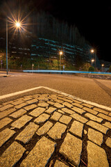 Cobblestone triangle covered by white lines and in the background the line of car lights