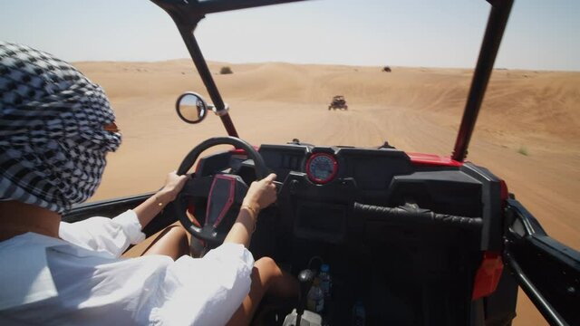Woman driving a sand dune buggy in the desert. Pov of young woman with covered head driving offroad vehicle in the desert