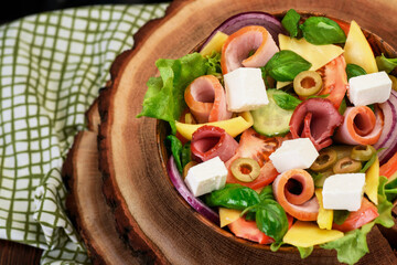 Salad with ham, tomatoes, feta and olives in a wooden bowl. Healthy food concept. Close-up