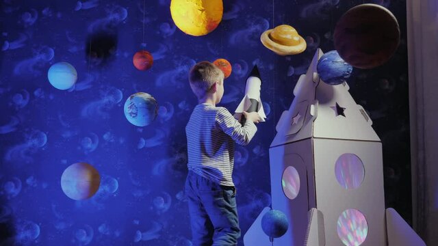 Little boy playing with toy rocket flying around the planets