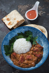 Blue bowl with butter chicken masala, white rice and indian flatbread, vertical shot on a brown stone background