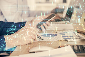 Double exposure of man's hands holding and using a digital device and forex graph drawing. Financial market concept.