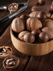 Walnuts and macadamia nuts in a bamboo bowl on wooden table with nutcracker in the background, vertical, close-up