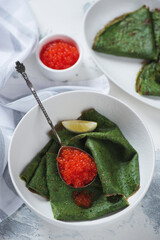 Green crepes with addition of spinach and red caviar, vertical shot on a white concrete background, selective focus