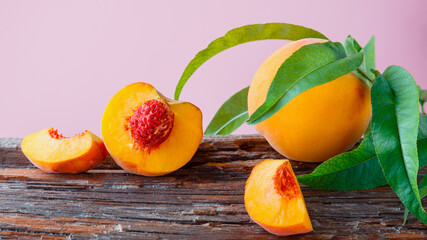 Peaches with leaves on wooden board. Peach in halves with bone, chopped pieces wedges peach halves. Ripe juicy peaches. Fresh organic peaches fruit on color pink background. Long web banner