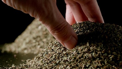 Male hand taking a pinch of dried basil from a pile