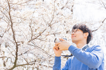 満開の桜をミラーレスカメラで撮影する男性