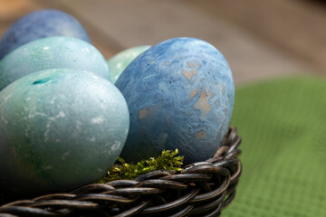Painted eggs in a wicker wooden basket on a kitchen table with a green towel in the background.