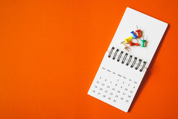 thumbtacks on white opened calendar with vivid grunge orange paper background , business or education concept