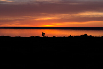 Fototapeta na wymiar sunset by the lake, red tint and a silhouette of two people looking at a beautiful background