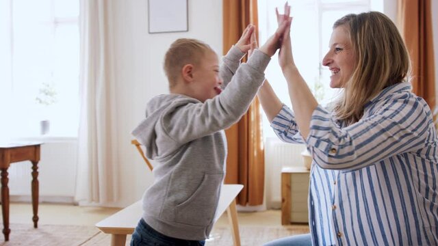 Single mother playing with down syndrome child at home, giving high five.