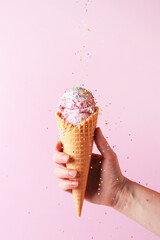 Female hand holding the pink ice cream with falling sprinkles in waffle cone