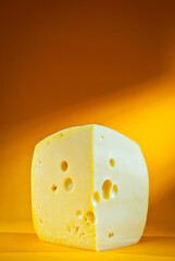 Yellow piece of cheese on an orange background. Triangular cheese close up. Copy space and free space for text near the cheese.