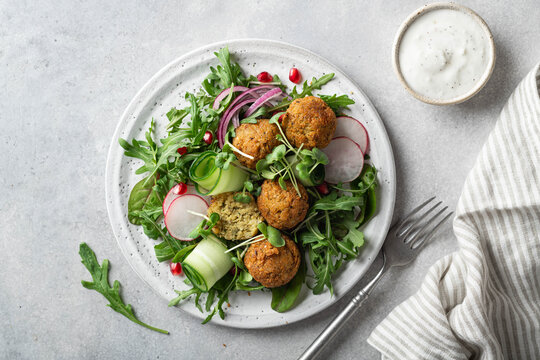 Falafel and fresh vegetables salad on a white ceramic plate on concrete background, top view. 