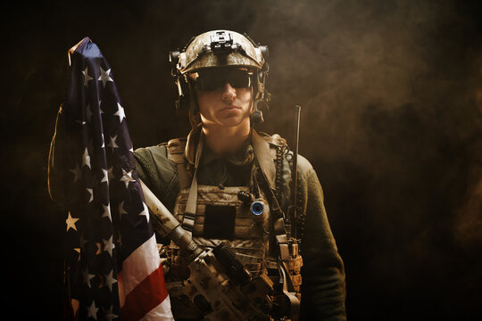 Special forces soldier holding US national flag in the dark