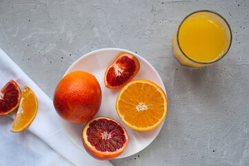 Sweet and juicy blood oranges and oranges, whole and cut on a white plate and gkasses of fresh...