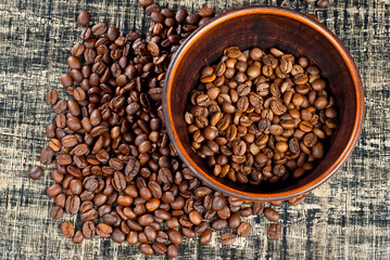 Coffee beans close up. Coffee in a clay bowl on a wooden board. Coffee texture on a black shabby table.
