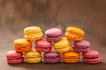 Fototapeta na wymiar Macaroons. Multicolored Macaroons on a brown background. Pyramid. Pink, yellow and red Macaroons. French cake. Place for your text.