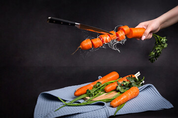 Whole and sliced ​​ripe carrots levitate on a black background Levitating knife cuts carrots Still life with carrots