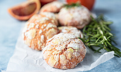 Homemade orange crinkle cookies with powdered sugar on baking paper, blue concrete background. Cracked citrus biscuits.
