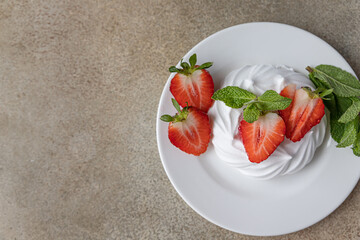 Mini Pavlova meringue cakes with strawberries and mint on a plate, concrete background.