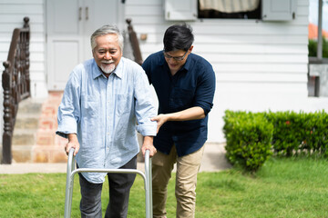 Elderly Asian father and Adult son walking in backyard. Positive Asian man caregiver helping patient
