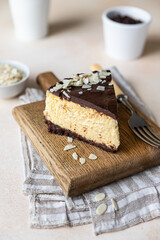 Slice of no baked creamy cheesecake with chocolate glaze and almond, light concrete background.