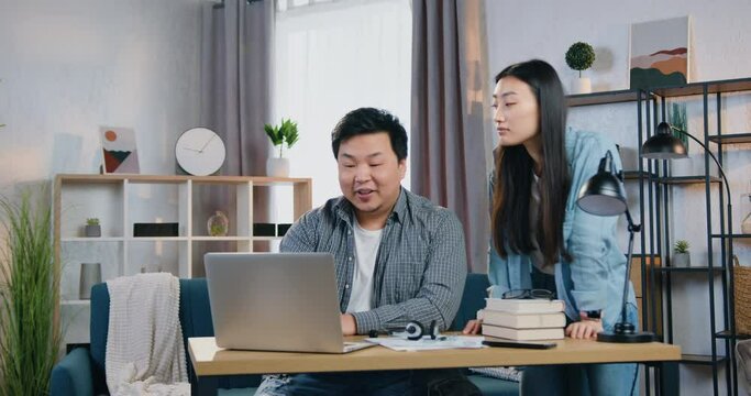 Attractive positive confident chinese man and woman working together on business project on computer in beautifully decorated office