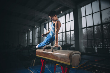 Fototapeta na wymiar Little male gymnast training in gym, flexible and active. Caucasian fit little boy, athlete in sportswear practicing in exercises for strength, balance.