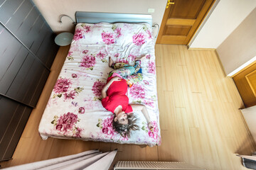 Pregnant woman in red t-shirt lies on the bed in the bedroom