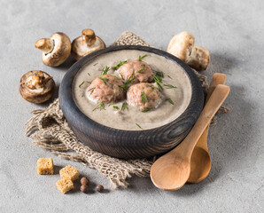 Vegan champignon soup puree with meatballs, dill and croutons in a wooden bowl on a linen napkin on a light gray background in rustic style