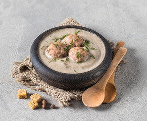 Mushroom soup puree with meatballs, dill and croutons in a wooden bowl on a linen napkin on a light gray background in rustic style
