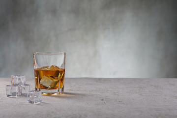 Whiskey im Glas mit Eiswürfel vor einer Betonwand
