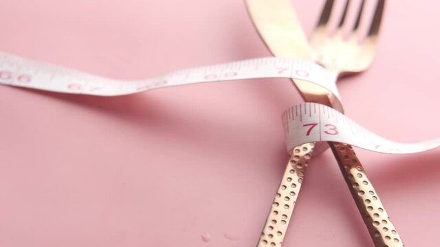 fork with measurement tape on pink background 