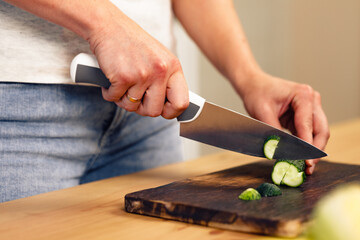 Hands of a woman cutting cucumber on wooden cutting board