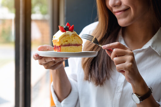 Closeup image of a beautiful young asian woman holding and eating a cake by fork