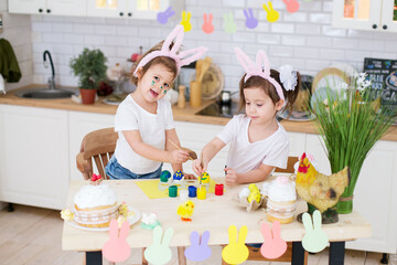 Two girls with bunny ears in the kitchen are decorating eggs for Easter. Easter holiday